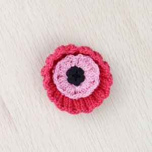 May include: A pink and red crocheted flower with a black button center.