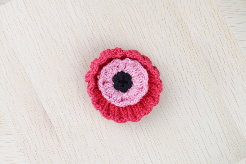 May include: A pink and red crocheted flower with a black button center.