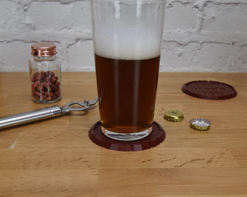May include: A glass of beer on a brown coaster with the words "Your Words Here" on it. There are two bottle caps and a bottle of peanuts on a wooden table.