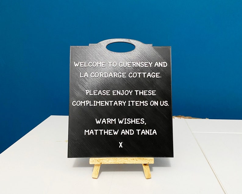 May include: Black chalkboard sign with white text that reads "Welcome to Guernsey and La Cordarge Cottage. Please enjoy these complimentary items on us. Warm wishes, Matthew and Tania X".