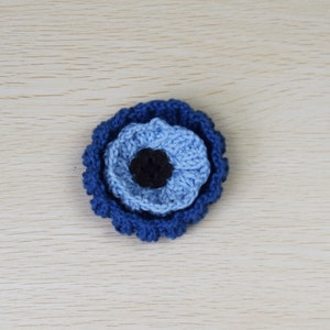 May include: A crocheted blue and black evil eye charm. The charm is made of yarn and has a round shape.