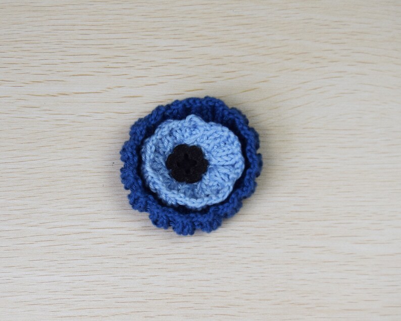 May include: A crocheted blue and black evil eye charm. The charm is made of yarn and has a round shape.