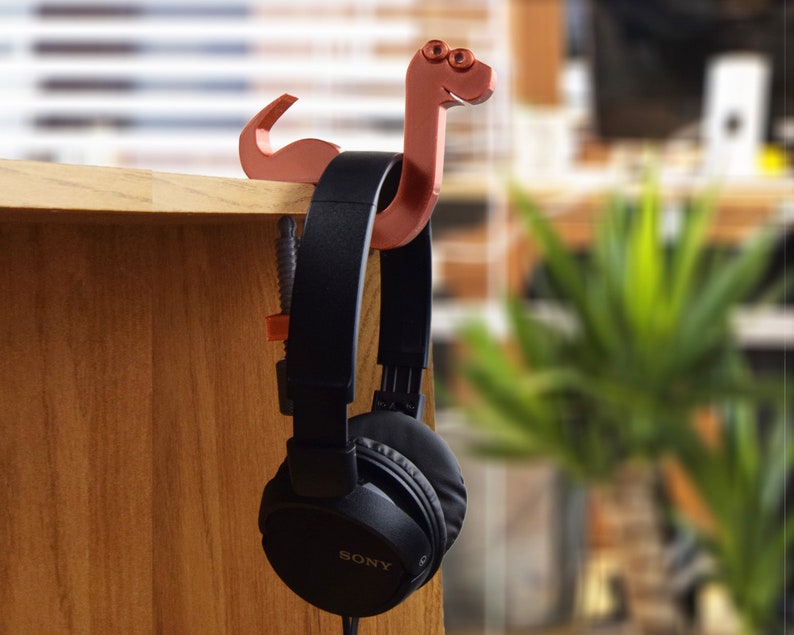 May include: A brown 3D printed snake-shaped headphone holder with a pair of black headphones hanging from it.