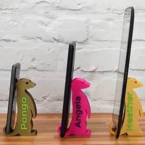 K&ouml;nnte beinhalten: Drei Handyst&auml;nder aus 3D-gedruckten Erdm&auml;nnchen, die jeweils ein Handy in unterschiedlicher Gr&ouml;&szlig;e halten. Die St&auml;nder sind gold, pink und braun. Die Namen "Pongo", "Angela" und "Heather" sind auf den St&auml;ndern aufgedruckt.