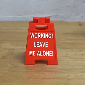 May include: A red plastic sign with the text "WORKING! LEAVE ME ALONE!" on it.