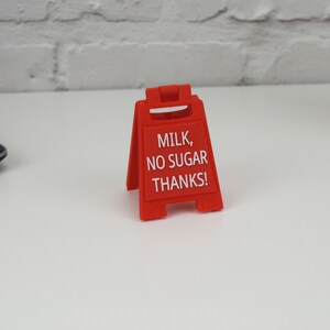 Może przedstawiać: Czerwony plastikowy znak z napisem "MILK, NO SUGAR THANKS!"