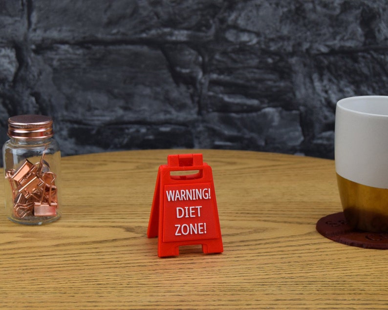 May include: Red warning sign with the text "WARNING! DIET ZONE!" on a wooden table.