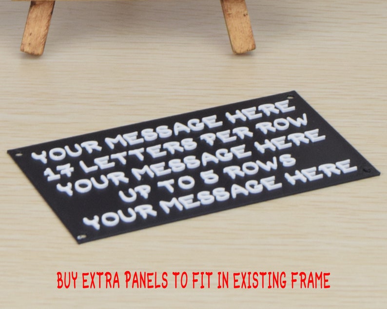 May include: Black sign with white raised letters that read "YOUR MESSAGE HERE 17 LETTERS PER ROW YOUR MESSAGE HERE UP TO 5 ROWS YOUR MESSAGE HERE". The sign is on a light wood surface. BUY EXTRA PANELS TO FIT IN EXISTING FRAME is written in red below the sign.