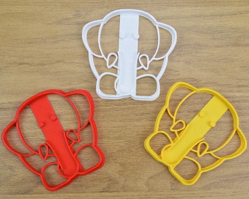May include: Three cookie cutters shaped like elephants. The cutters are red, yellow, and white.