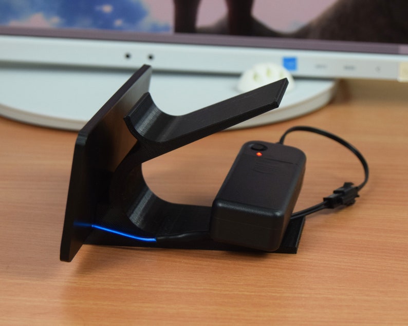 Pu&ograve; includere: Un supporto nero stampato in 3D con una striscia di luce LED blu. Il supporto &egrave; collegato a un adattatore di alimentazione nero con un indicatore LED rosso.