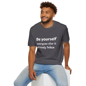 K&ouml;nnte beinhalten: Ein dunkelgraues T-Shirt mit dem Text "Be yourself everyone else is already taken" in Wei&szlig;.
