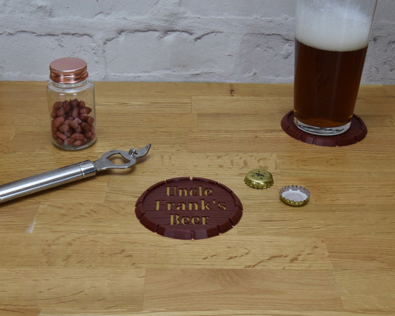 May include: A brown wooden coaster with the text "Uncle Frank's Beer" engraved on it. There are two bottle caps and a bottle opener on a wooden table.