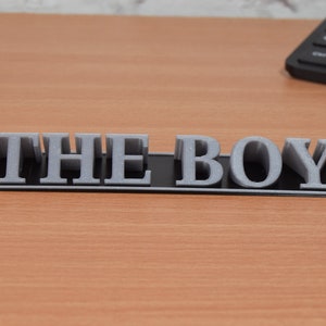May include: A black plaque with the words "THE BOY" in raised silver letters.
