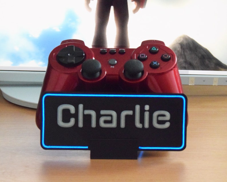 Pu&ograve; includere: Un controller per videogiochi rosso con una base nera e un cartello al neon blu che dice "Charlie".