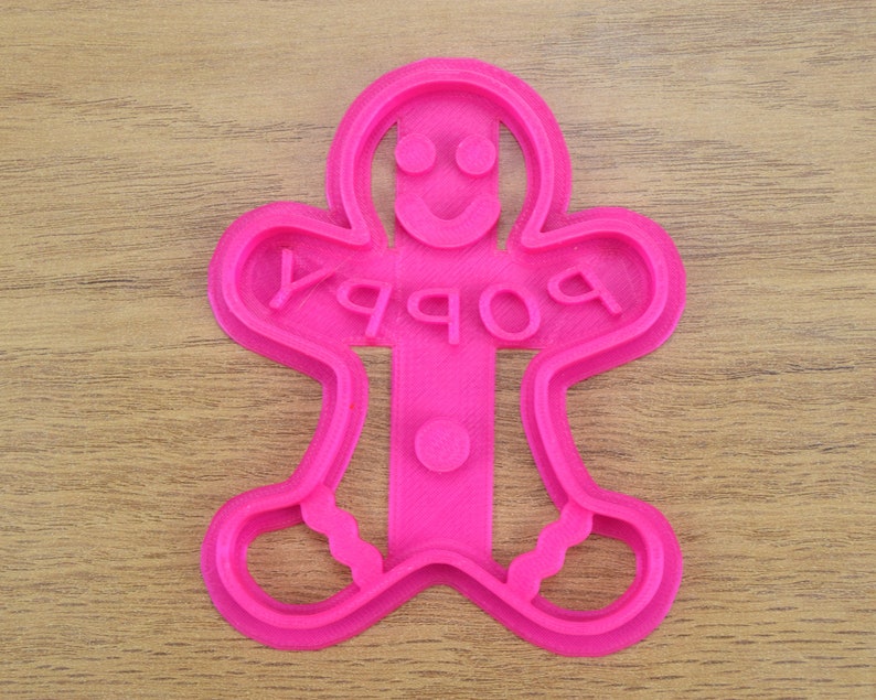 Puede incluir: Cortador de galletas de jengibre de pl&aacute;stico rosa con la palabra "Happy" escrita en &eacute;l.