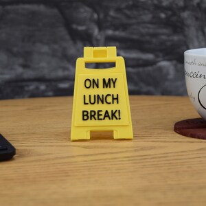 Może przedstawiać: Ż&oacute;łty znak ostrzegawczy z czarnym tekstem, kt&oacute;ry brzmi "On My Lunch Break!"