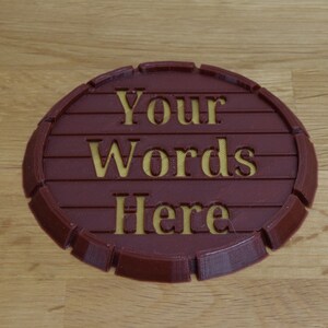 May include: A round, brown, 3D printed coaster with a raised edge. The coaster has the words "Your Words Here" engraved in yellow.