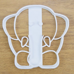 May include: White plastic cookie cutter shaped like an elephant with a simple design. The elephant has large ears, a trunk, and a small tail.