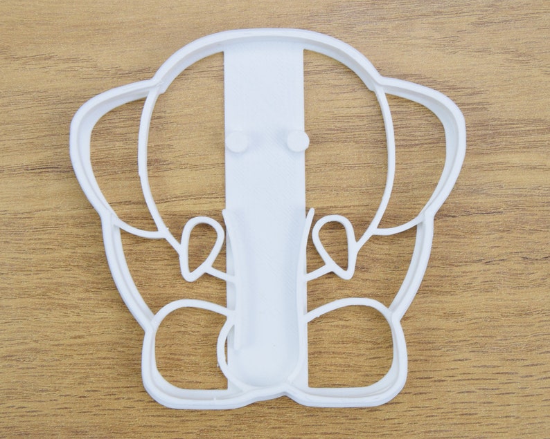 May include: White plastic cookie cutter shaped like an elephant with a simple design. The elephant has large ears, a trunk, and a small tail.