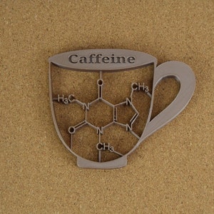 May include: A silver-colored, cup-shaped object with the word "Caffeine" at the top. The interior of the cup features a molecular structure diagram. The cup is set against a textured, tan background.