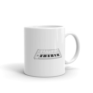May include: White ceramic mug featuring a black line drawing of a vintage synthesizer with a keyboard.
