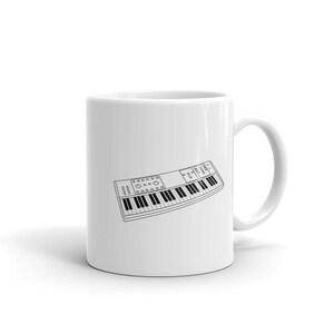 May include: A white ceramic mug featuring a black line drawing of a keyboard.