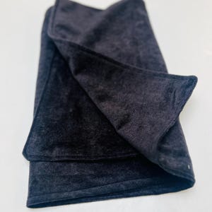 May include: A folded, dark grey velvet scarf. The scarf is rectangular with a soft, plush texture. The edges are neatly finished, and the fabric drapes gently. The scarf is a solid colour, with no visible patterns or embellishments.
