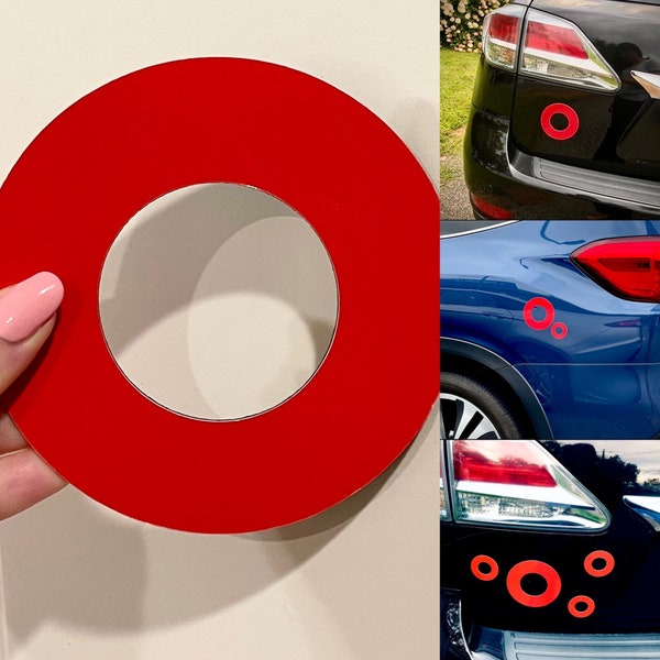 以下が含まれることがあります： 赤いビニール製のリング型のステッカー。ステッカーは白い背景と車の後ろに表示されています。ステッカーは、赤いリングと内側に小さな赤いリングがあるシンプルなデザインです。