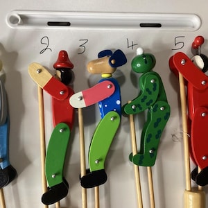 May include: Five wooden stick puppets labeled 1 through 5, featuring a rabbit, a character with a red hat, a blue-eared animal, a green spotted creature, and a red figure with antennae. Each puppet is attached to a wooden stick for movement.
