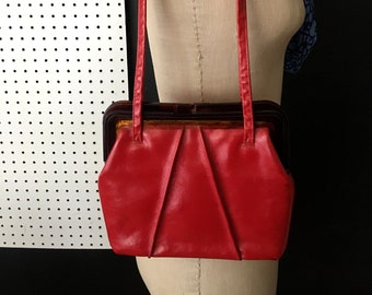 May include: A red leather purse with a brown plastic frame and a long red strap.