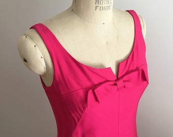 May include: A sleeveless, hot pink dress with a bow at the neckline. The dress has a fitted bodice and a flowing skirt.