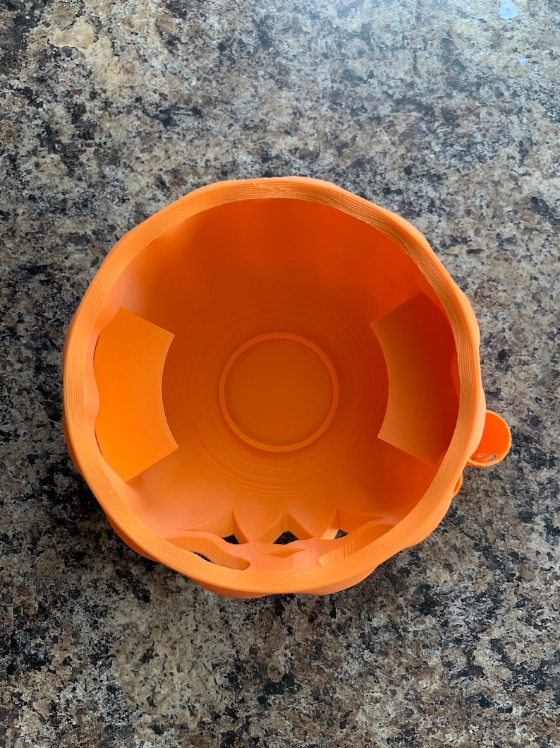 Puede incluir: Taz&oacute;n de pl&aacute;stico naranja en forma de calabaza con un dise&ntilde;o tallado alrededor del borde. El taz&oacute;n tiene un interior liso y redondeado.
