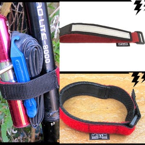 Puede incluir: Correa negra y roja para accesorios de bicicleta con una tira blanca reflectante y una hebilla negra. La correa está envuelta alrededor de un cuadro de bicicleta, sujetando un bote rojo, una palanca de neumático azul y una cámara de aire negra. La marca "MOUNT ZOOM" es visible.