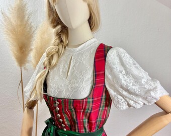 May include: A traditional German dirndl dress. The dress features a red and green plaid bodice with silver buttons, a white lace blouse, and a green satin skirt. A green velvet headband and a green satin sash complete the outfit.