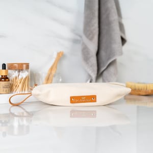 May include: A white canvas zippered pouch with a brown leather handle and a brown leather patch that says "The Pretty Owl".