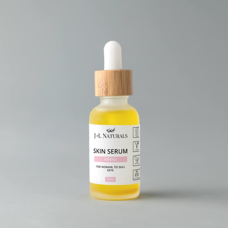 May include: A clear glass bottle with a bamboo lid and a yellow liquid inside. The bottle is labelled "J'L Naturals Skin Serum Shine For Normal to Dull Skin 1.0 fl oz".