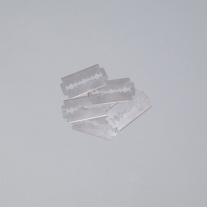 May include: A close-up of a pile of six silver razor blades.