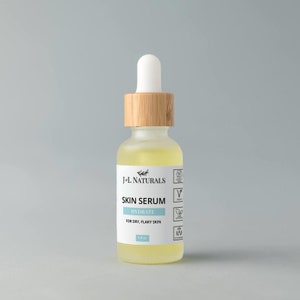 May include: A clear glass bottle with a bamboo lid and a white dropper top. The bottle contains a yellow liquid and has a white label that reads "J+L NATURALS SKIN SERUM HYDRATE FOR DRY, FLAKY SKIN 1.0 oz". The label also has several icons, including a vegan symbol, a cruelty-free symbol, and a natural ingredients symbol.