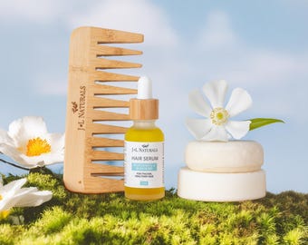 May include: A wooden comb, a bottle of J+L Naturals Hair Serum, and two white solid shampoo bars on a bed of green moss. The bottle is labeled "J+L Naturals Hair Serum, Peppermint & Rose Leaf, For Thicker, Healthier Hair".
