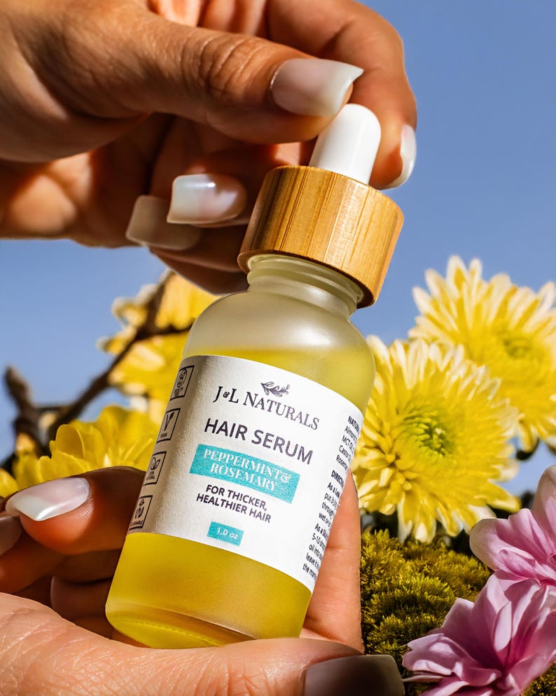 May include: A clear glass bottle with a bamboo lid and a dropper. The bottle contains a yellow liquid and has a white label that reads "J&L Naturals Hair Serum Peppermint & Rosemary For Thicker, Healthier Hair 1.0 oz".