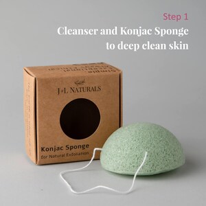 K&ouml;nnte beinhalten: Ein gr&uuml;ner Konjak-Schwamm mit einer wei&szlig;en Schnur daran. Der Schwamm liegt auf einer grauen Oberfl&auml;che neben einem braunen Karton mit dem Text "J&L NATURALS" und "Konjac Sponge for Natural Exfoliation".