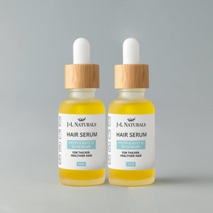 May include: Two amber glass bottles with bamboo lids and white dropper tops. The bottles contain a yellow liquid and have white labels with the text "J-L Naturals Hair Serum Peppermint & Rosemary For Thicker, Healthier Hair 1.0 oz."