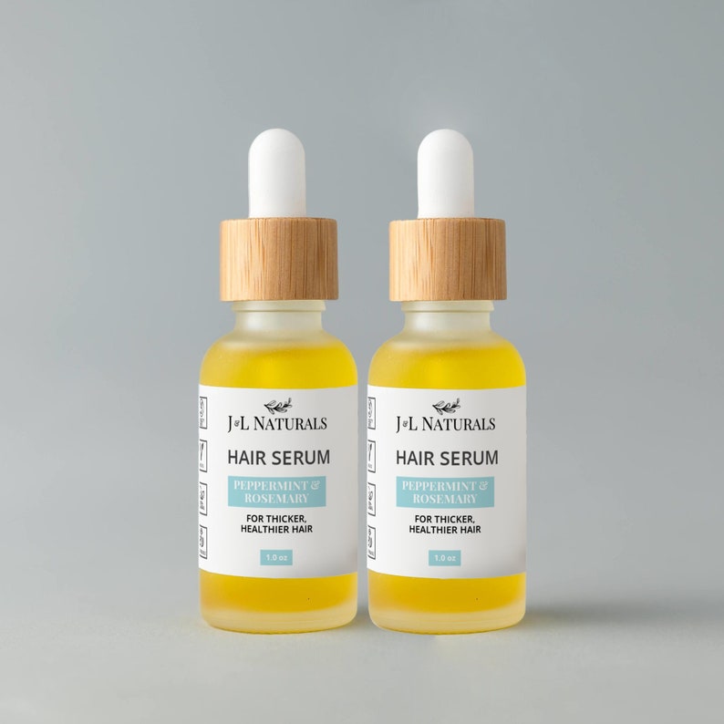 May include: Two amber glass bottles with bamboo lids and white dropper tops. The bottles contain a yellow liquid and have white labels with the text "J-L Naturals Hair Serum Peppermint & Rosemary For Thicker, Healthier Hair 1.0 oz."