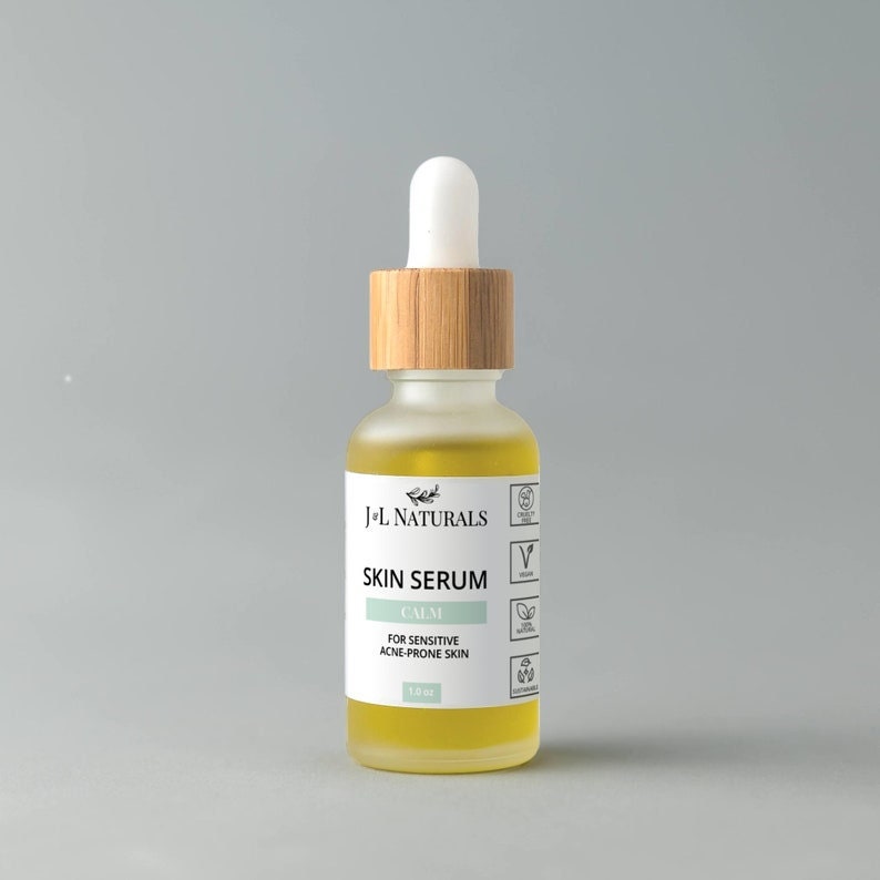 May include: A clear glass bottle with a bamboo lid and a white dropper. The bottle contains a yellow liquid and has a label that reads "J+L NATURALS SKIN SERUM CALM FOR SENSITIVE ACNE-PRONE SKIN 1.0 oz".