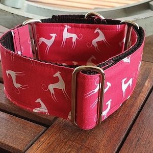 Könnte beinhalten: Ein rotes Hundehalsband mit weißen Silhouetten von Windhunden darauf gedruckt. Das Halsband hat zwei silberne Metallschnallen.