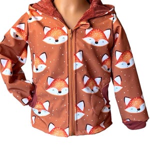 以下が含まれることがあります： 漫画のキツネの繰り返し模様が特徴の茶色のフード付きジャケット。 ジャケットはフルジッパー、ポケット、フードと袖口にはコントラストの効いた錆色の裏地が付いています。 白い水玉模様が生地全体に散りばめられています。