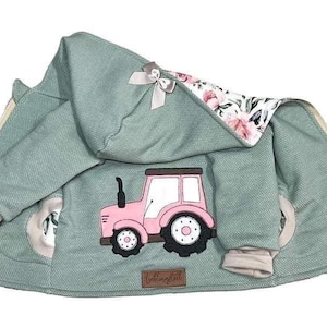 Può includere: Una giacca verde con cappuccio con un design di trattore rosa sul davanti. La giacca ha una fodera floreale e una chiusura a zip. Il testo "tollypot" è visibile sul fondo della giacca.