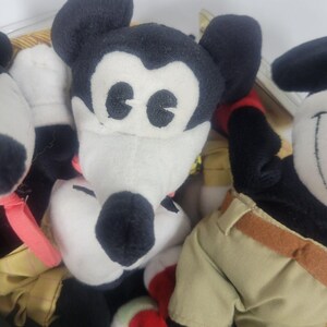 May include: Close-up of several Mickey Mouse plush toys. The toys have black ears, black and white faces, and black noses. One toy is in the foreground, with others partially visible in the background. The toys are in a basket.
