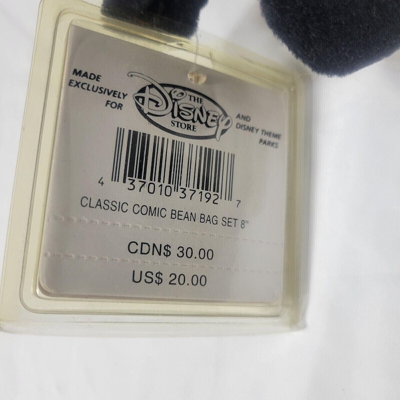 May include: A clear plastic tag with the Disney Store logo and text that reads "CLASSIC COMIC BEAN BAG SET 8". The tag is attached to a black plush toy. The tag also has a barcode.