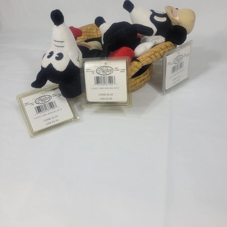 May include: A collection of Disney plush bean bag toys, including Mickey Mouse and other characters, are displayed in a woven basket. Each toy has a tag attached. The toys are black, white, red, and tan.